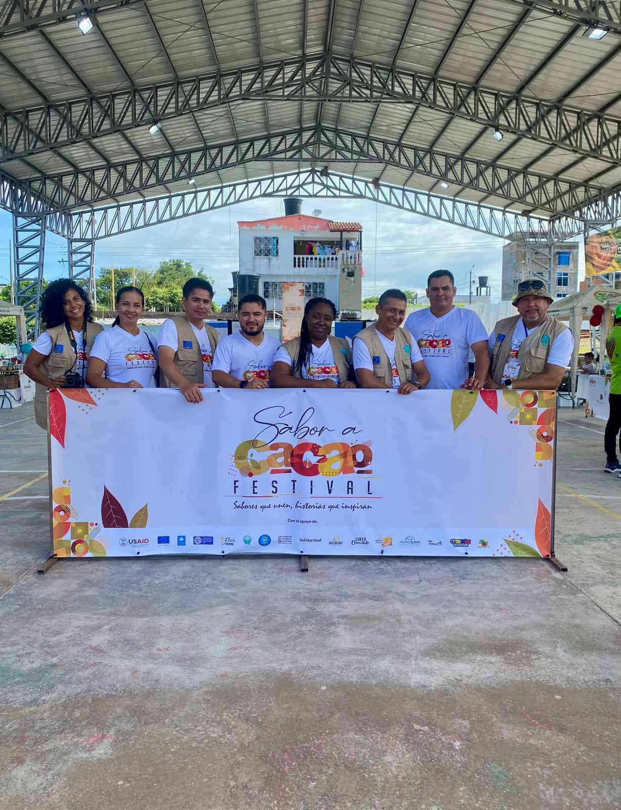 Organizadores del Festival Sabor a Caco de Colombia posando a la entrada del recinto con una pancarta del evento.